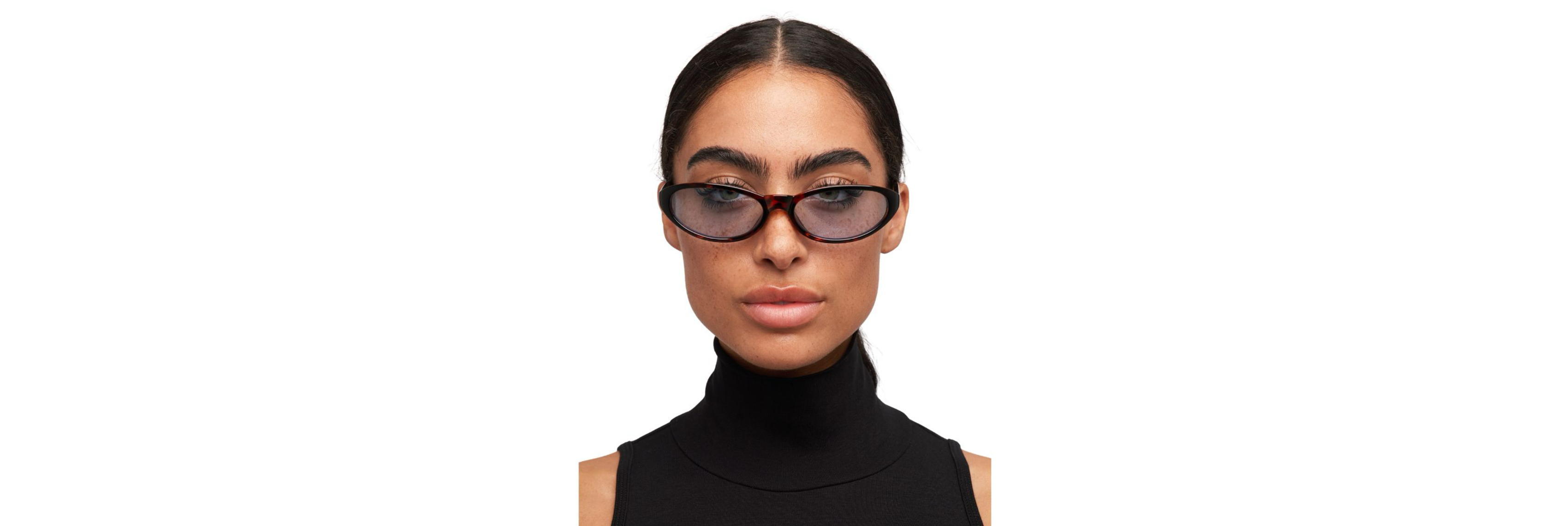 Two festival looks laid out on a blanket—one pair of dark smoke‑fade sunglasses and one pair of warm brown‑tint cat‑eyes—next to a tiny crossbody bag, phone, and ticket wristband a