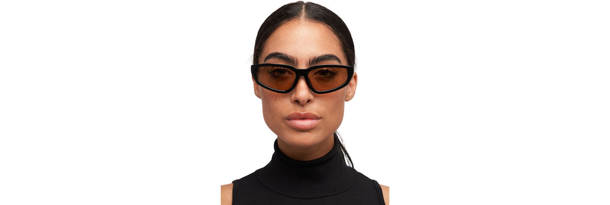 Hands gently checking sunglass fit at the bridge and temples on a bright vanity, with a soft pouch and cleaning cloth nearby.