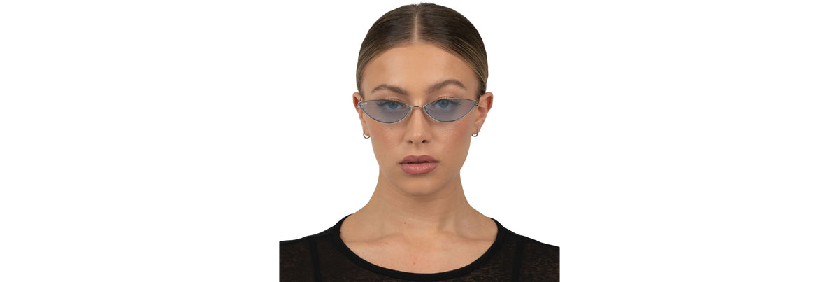 A traveler at a laptop in a softly lit airport lounge wearing subtle cat‑eye blue‑light glasses next to a carry‑on and coffee.