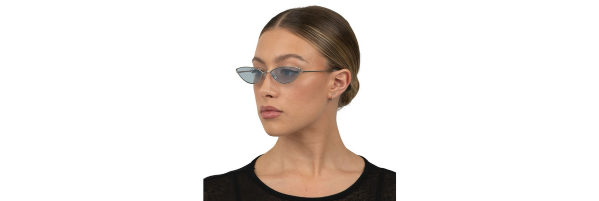 Two pairs of OTRA sunglasses on a city windowsill—one medium‑tint pair for shade and one darker pair for bright sun—with skyline and sunlit street below.