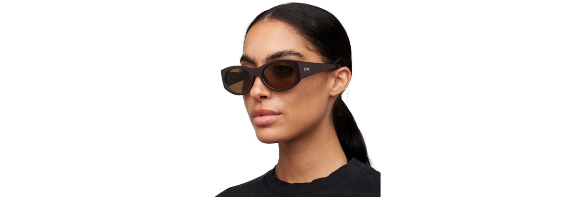 A woman in thin metal rectangle sunglasses and a neutral blazer stepping from desk to subway platform, showing a light, minimal silhouette.