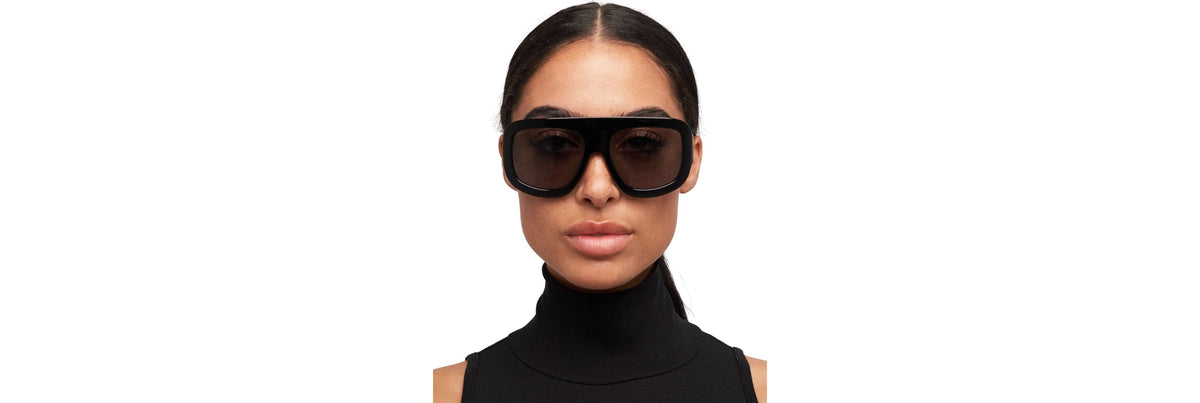 Model wearing bold square sunglasses with a low bun and small gold hoops, showing balanced proportions between frames, hairstyle, and accessories.