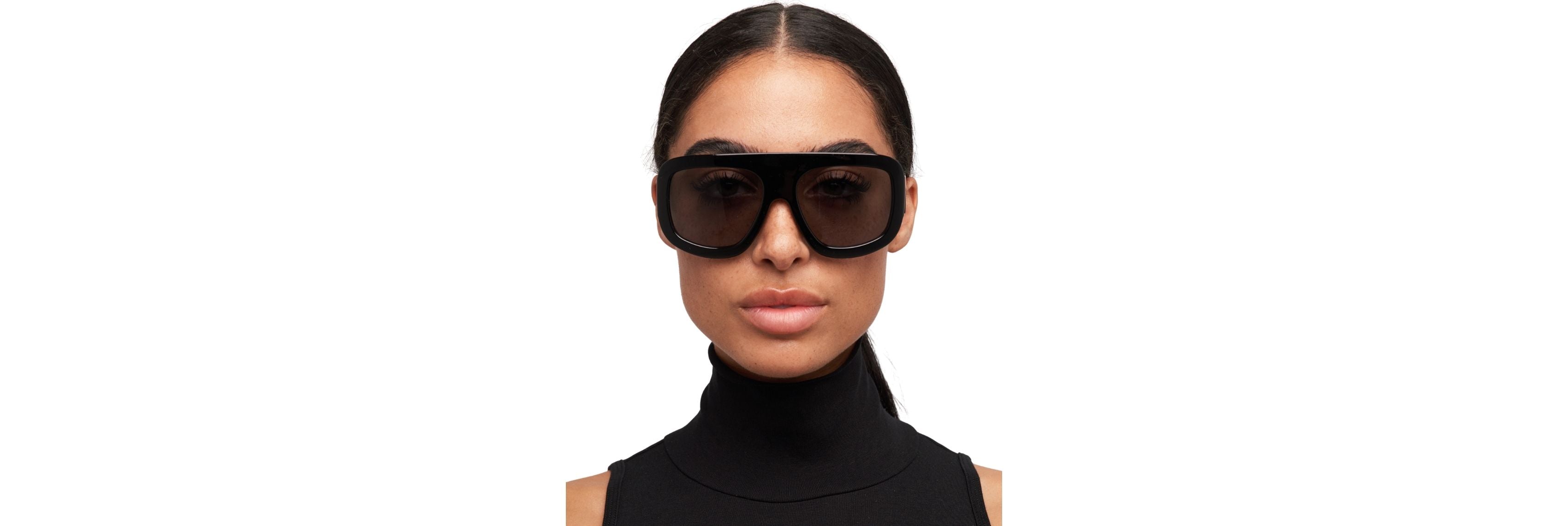 Model wearing bold square sunglasses with a low bun and small gold hoops, showing balanced proportions between frames, hairstyle, and accessories.