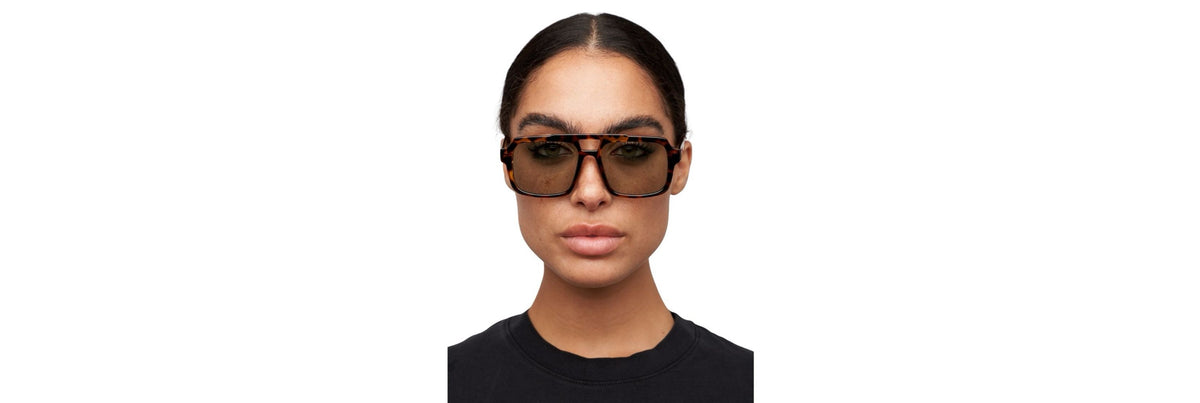 Open carry-on with clothing rolled and two sunglasses: one classic tortoiseshell pair and one darker sportier pair, plus a slim hard case.