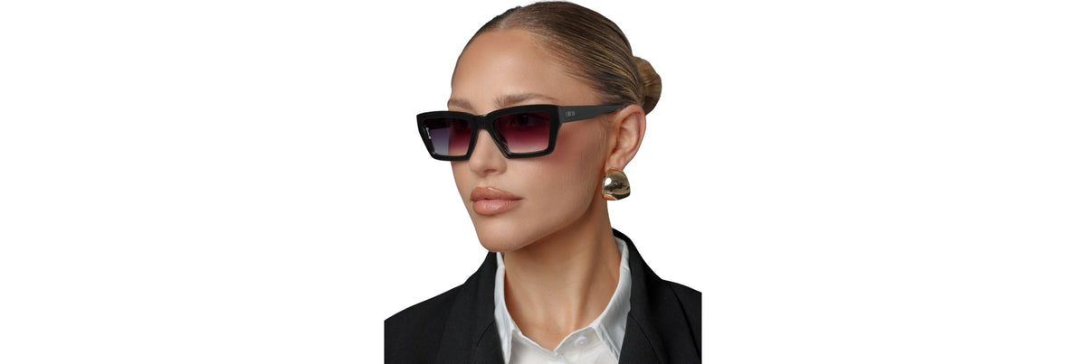 Close crop of a woman on a sunny coastal boardwalk wearing gently wrapped rectangular sunglasses that contour her cheeks and temples, showing stable coverage without a bulky sport