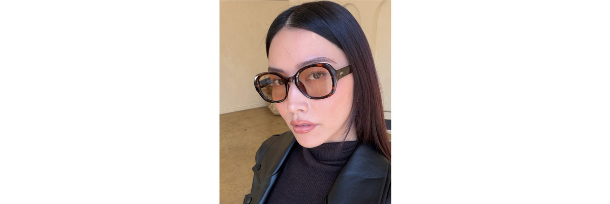 Close-up of two sunglasses on a table—one slim metal frame with adjustable silicone pads and one sculpted acetate frame with a saddle bridge—showing how each contacts a low bridge