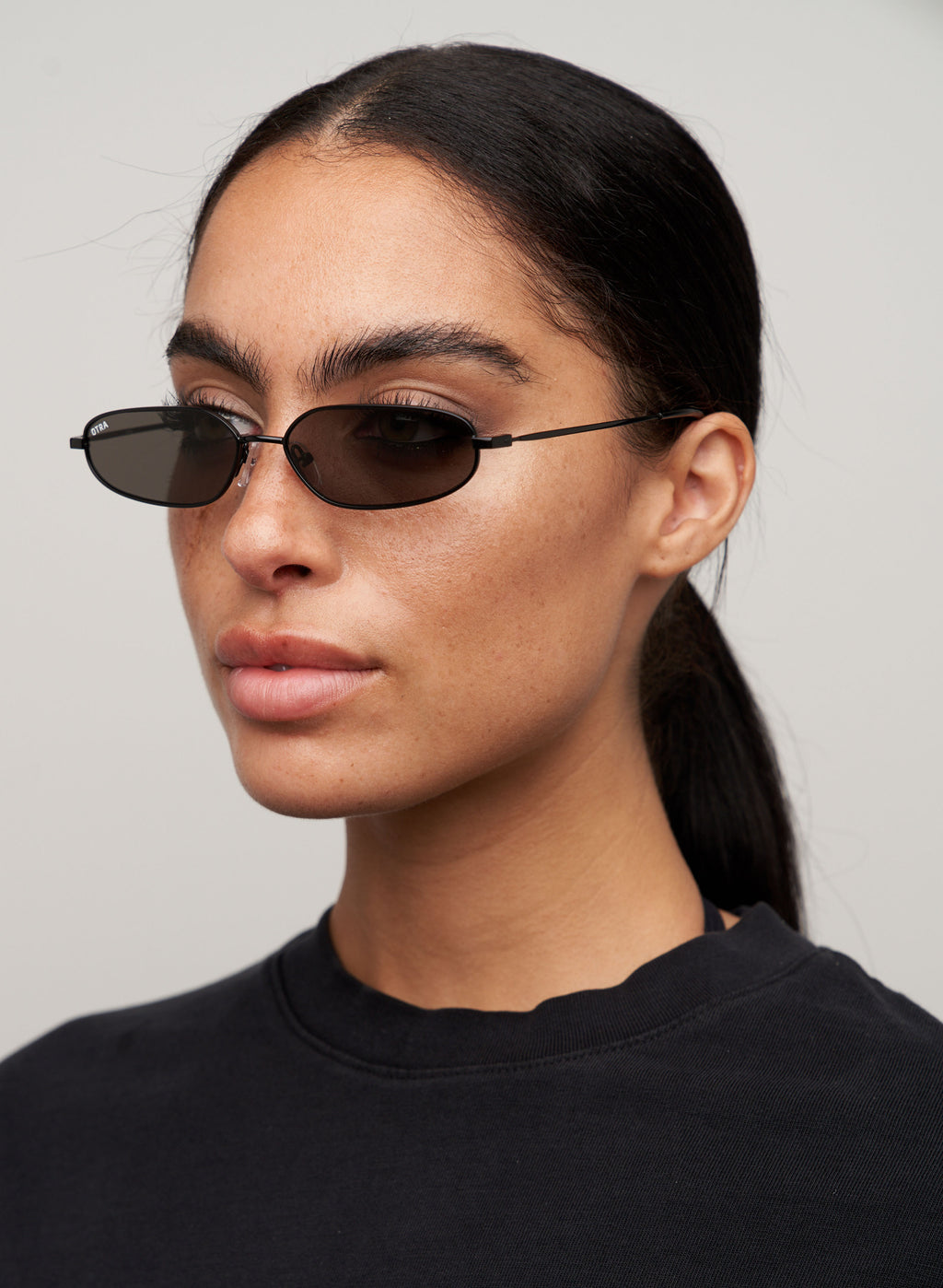 Otra Eyewear- Drew-Black- Three-quarter profile view of a model wearing the Drew - Black sunglasses, featuring a thin, minimal metal rectangular frame in black with a super 90s-inspired silhouette