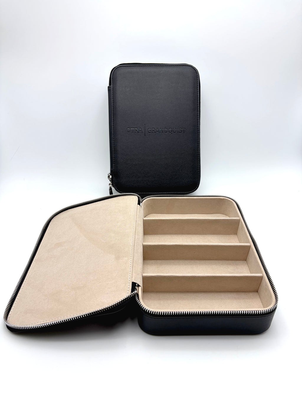 Otra Eyewear - GQ Travel Case - A black zippered jewelry organizer case shown open, with a beige interior featuring five compartments and a matching closed case standing upright in the background.