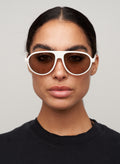Otra Eyewear - IGGY - Vanilla/Brown - Model wearing IGGY sunglasses in Vanilla/Brown featuring a high-gloss vanilla cream aviator frame, classic double bridge, and light brown lenses. Front-facing editorial portrait showcasing the timeless everyday silhouette with a clean, modern aesthetic in grey background.