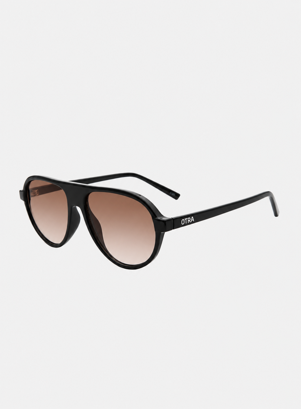 Otra Eyewear - IGGY - Black/Light Brown Fade - Angled view of IGGY sunglasses in Black/Light Brown Fade featuring a high-gloss black aviator frame, classic double bridge, and light brown gradient lenses, displayed against a clean grey background. A timeless everyday design with modern styling and full UV protection 