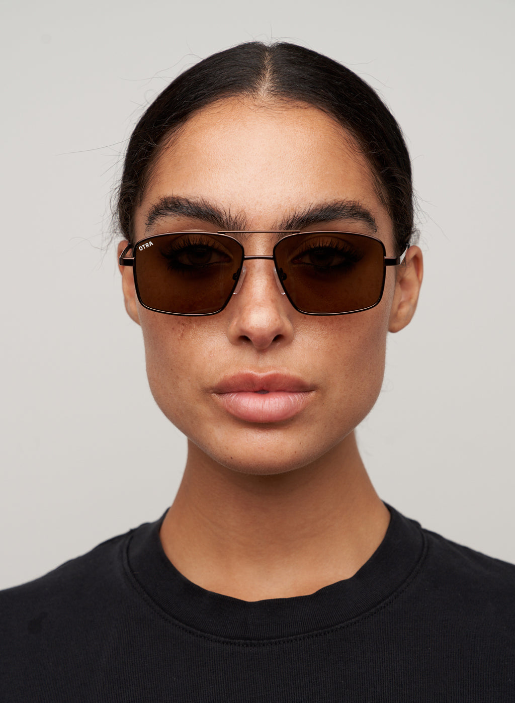 Otra Eyewear - NASH - Chocolate/Brown - Model wearing a NASH sunglasses in Chocolate/Brown featuring a sleek chocolate metal square aviator frame, warm brown lenses, and a refined double-bridge design, displayed against a clean grey background. A modern aviator style with lightweight construction and timeless everyday appeal.
