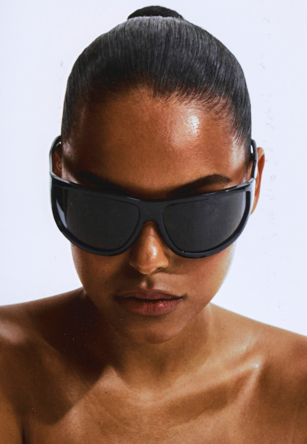 Otra Eyewear - Melanite - Black/ Smoke - Model wearing an oversized wrap sunglasses in black with dark smoke lenses, featuring a sculpted frame and a sleek sport-luxe silhouette.