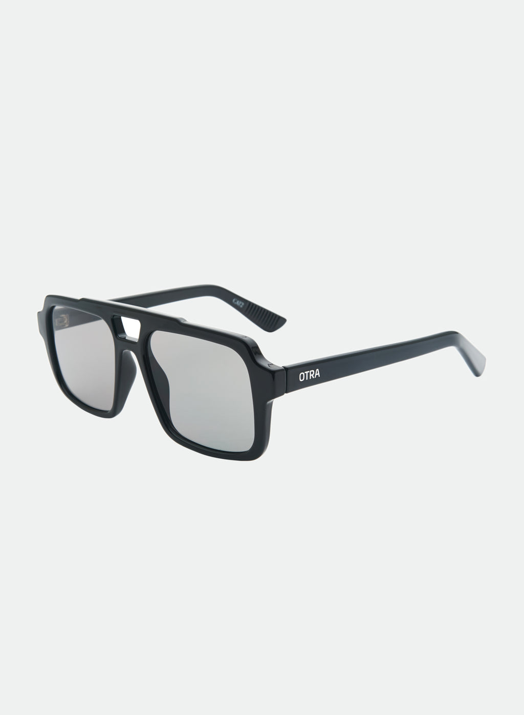 Otra Eyewear - TAME - Black/Smoke - Angled view of a TAME sunglasses in Black/Smoke featuring a lightweight black square aviator frame, dark smoke lenses, and a structured angular silhouette. A modern interpretation of the classic aviator designed for effortless everyday style in grey background