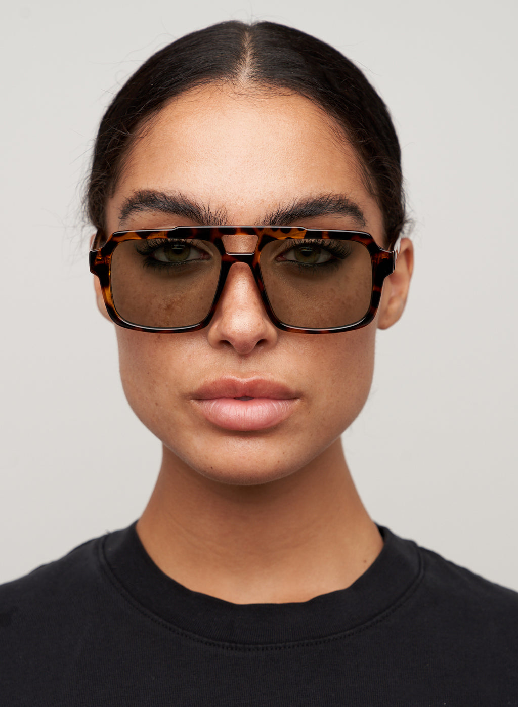 Otra Eyewear - TAME - Tort/Light Green - Model wearing a TAME sunglasses in Tort/Light Green featuring a lightweight tortoiseshell square aviator frame, light green lenses, and a structured angular silhouette. A modern interpretation of the classic aviator designed for effortless everyday style.